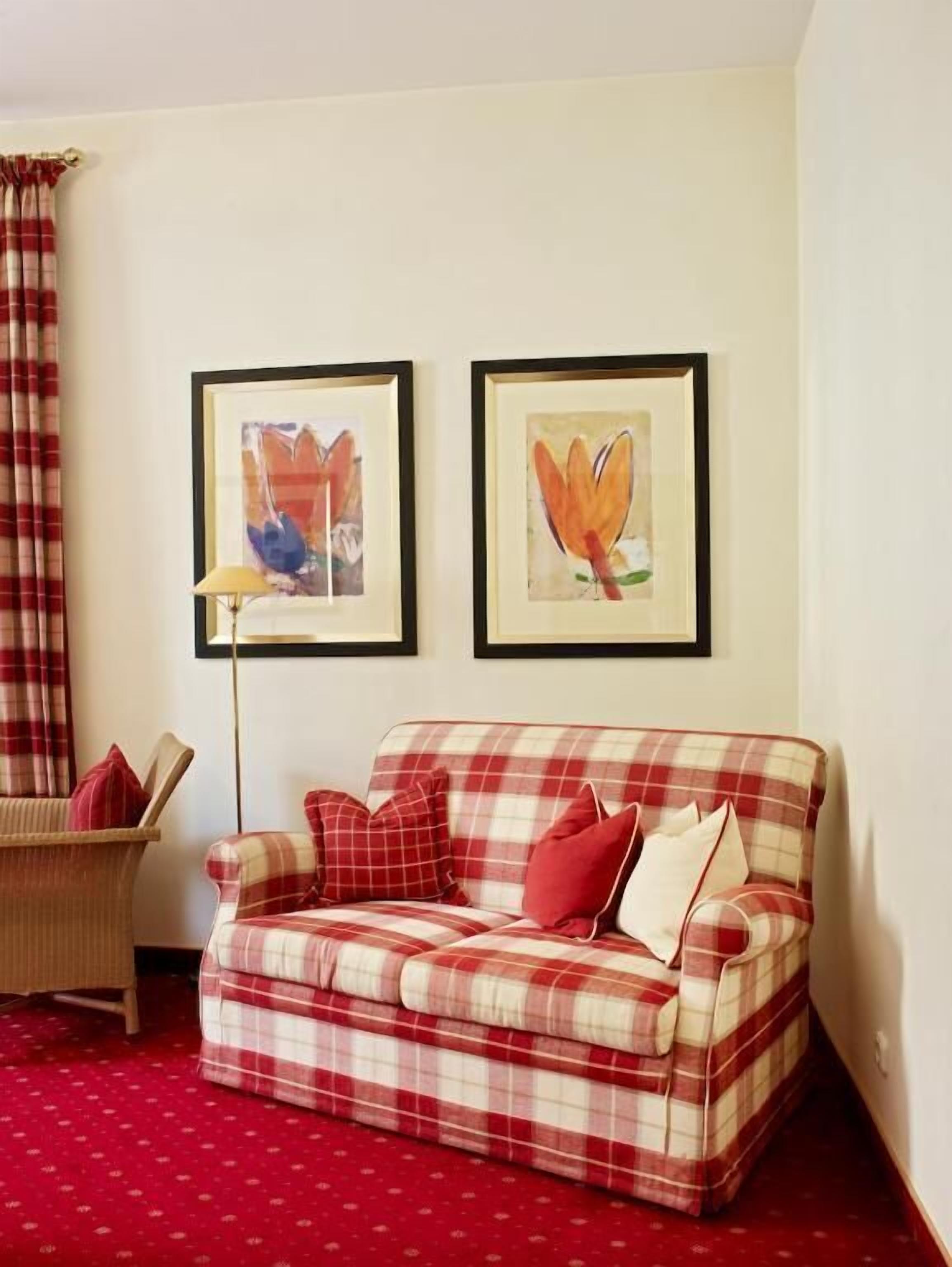 Una sala de estar con un sofá a cuadros, dos cuadros con motivos florales, una lámpara y un sillón.