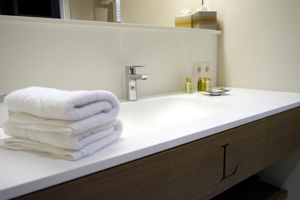 Ein Badezimmer mit einem weißen Waschbecken, einem Spiegel und einem Stapel weißer Handtücher.