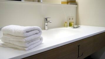 Ein Badezimmer mit einem weißen Waschbecken, einem Spiegel und einem Stapel weißer Handtücher.