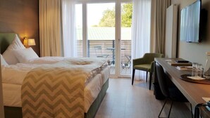 A hotel room with a bed, a desk, a chair, a TV, and a balcony with a table and chairs. - Romantik Hotel Das Lindner (Bad Aibling)