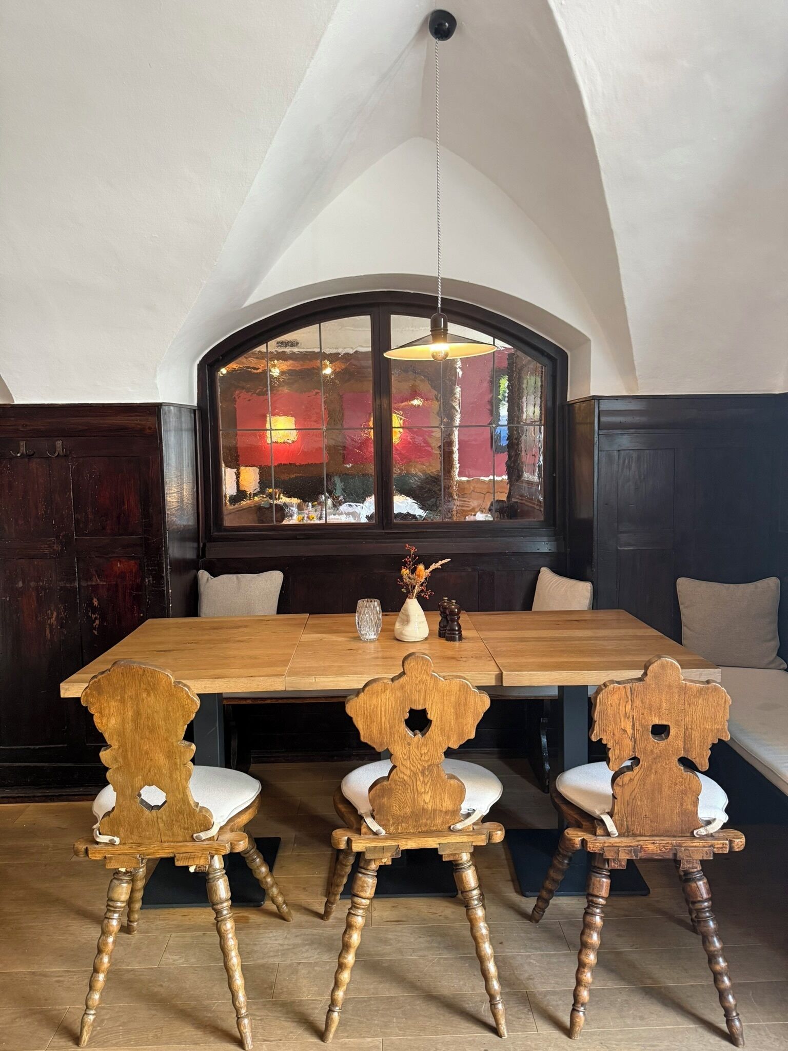 Un coin repas avec une table en bois, quatre chaises, un vase et une vue par la fenêtre.