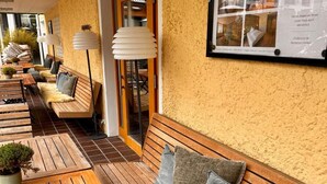 A cozy outdoor seating area with wooden benches and tables, a textured wall, and a framed picture. - Romantik Hotel Das Lindner (Bad Aibling)