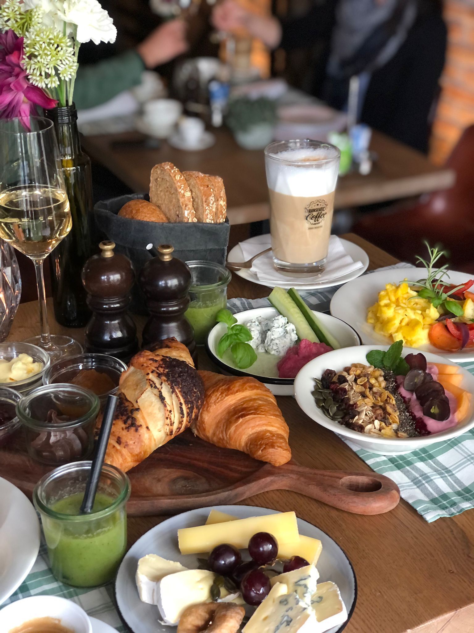 Una mesa de comedor con diversos alimentos, como pan, queso y un croissant, además de bebidas y salsas.