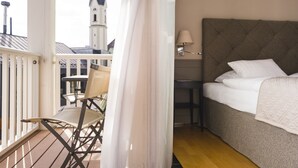 A hotel room with a bed, a chair, a table, and a view of a tower. - Romantik Hotel Das Lindner (Bad Aibling)
