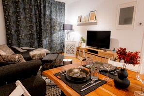Una sala de estar moderna con un sofá, una mesa de comedor dispuesta con platos, vasos y cubiertos, y un televisor de pantalla plana montado en la pared.