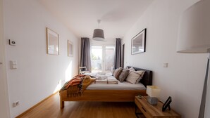 A modern bedroom with a wooden bed, a bedside table with a lamp, and a view of the outdoors through a window.