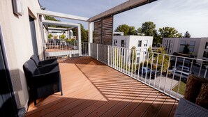A balcony with a wooden floor, white railing, and a black chair.