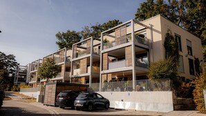 A multi-story residential building with balconies, a gated entrance, and parked cars.