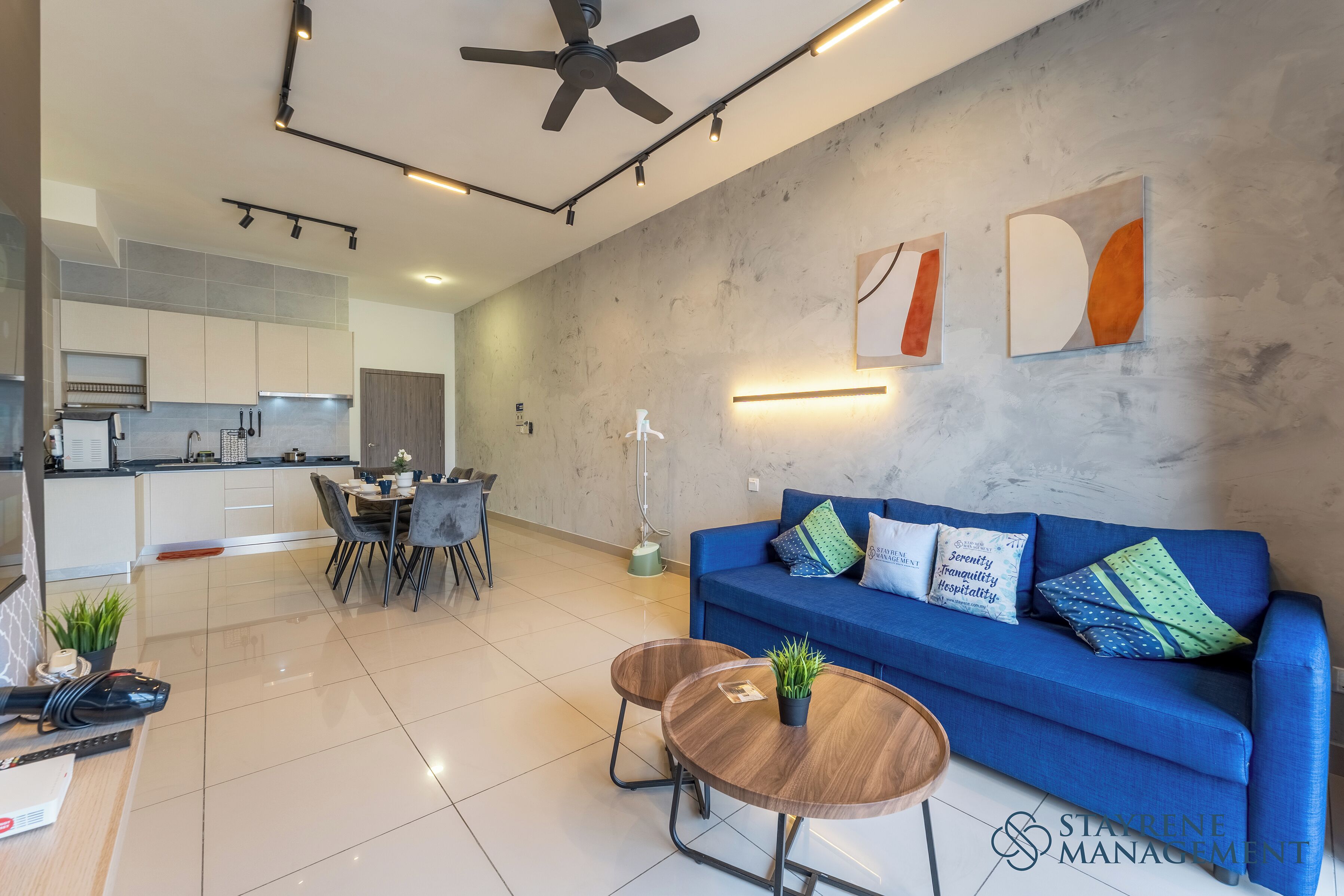 A modern living space with a blue sofa, a dining table, and a kitchen area.