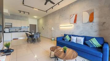 A modern living space with a blue sofa, a dining table, and a kitchen area.