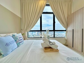 A hotel room with a large bed, beige curtains, a view of a cityscape, and a logo for Stayrene Management.