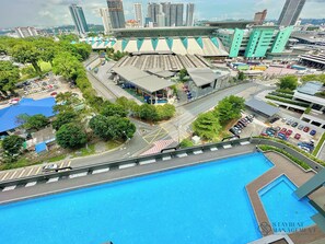 A hotel with a swimming pool, a parking area, and a view of a cityscape with tall buildings.