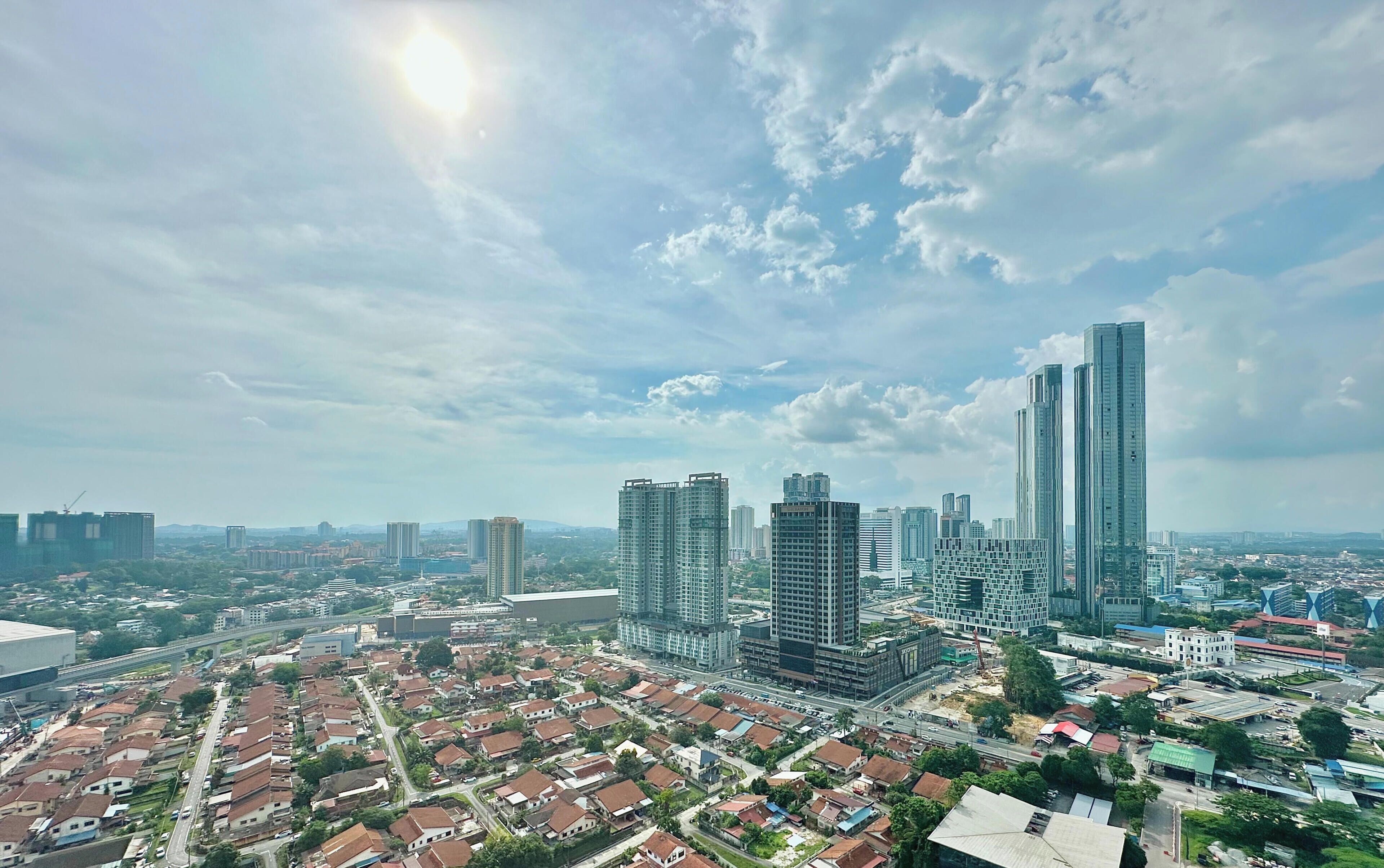 A cityscape with high-rise buildings, a residential area with houses, and a clear sky.