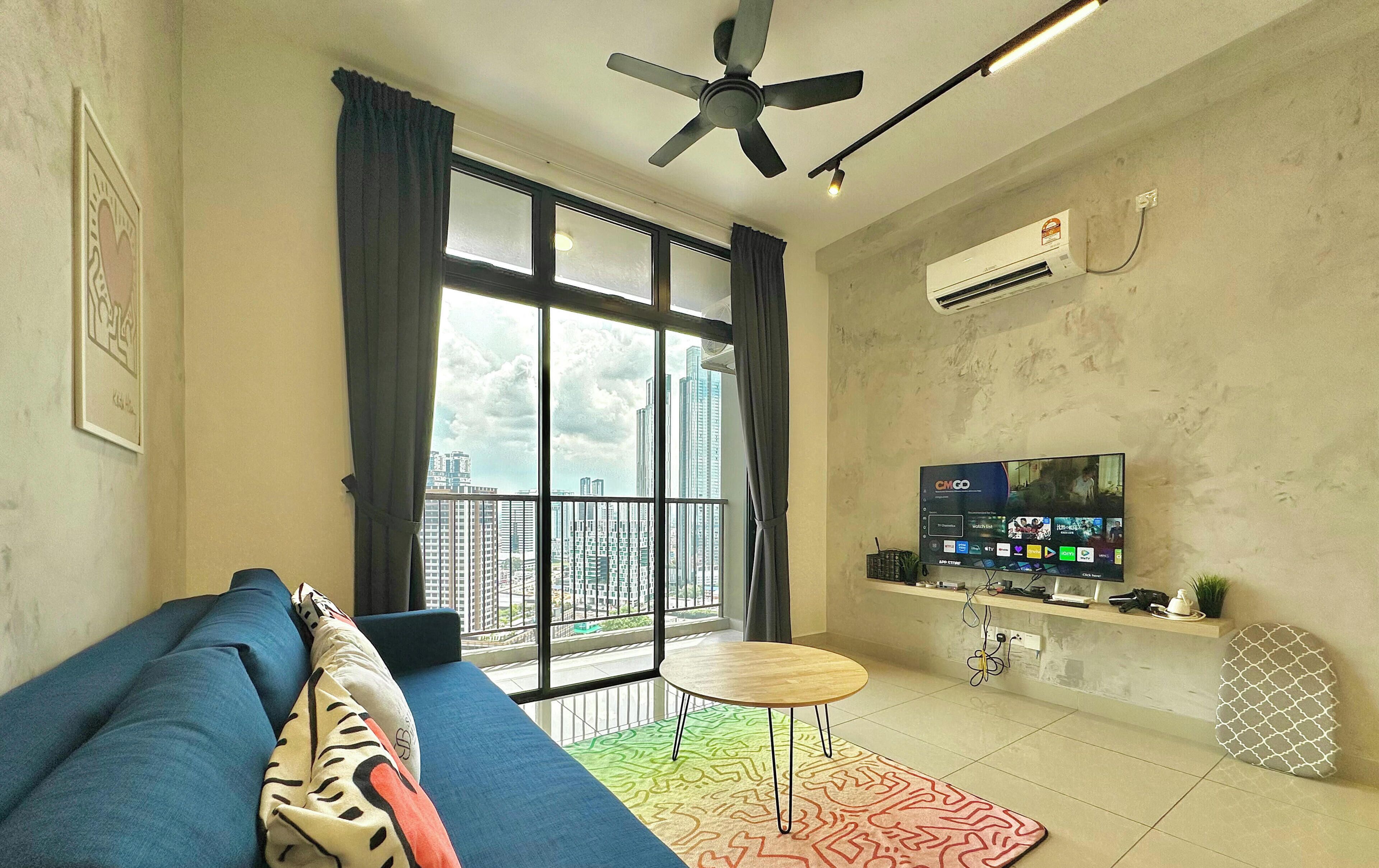 A modern living room with a blue sofa, a small round table, a ceiling fan, and a large window with curtains.