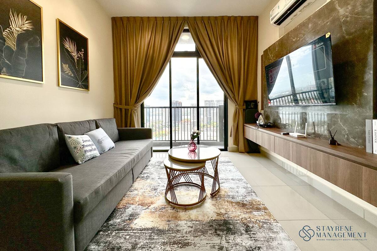 A modern living room with a grey sofa, a round coffee table, and a large TV mounted on the wall.