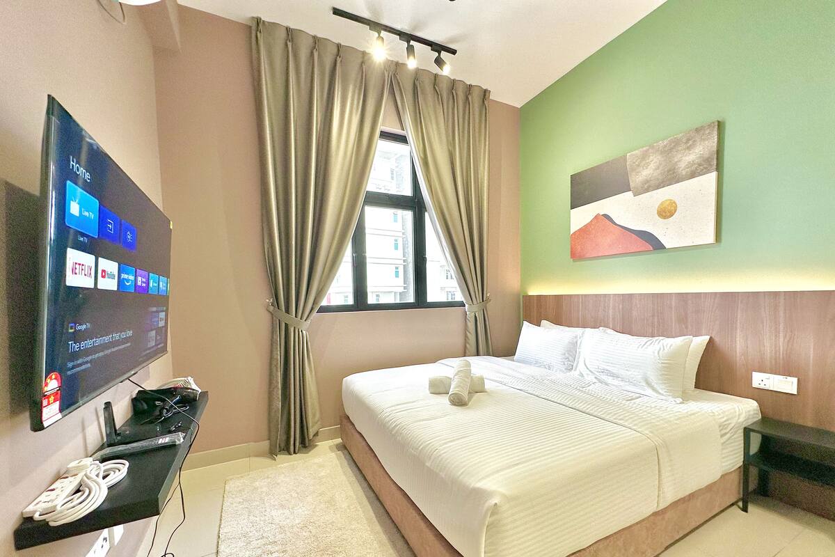 A hotel room with a bed, a flat-screen TV displaying streaming services, a window with curtains, and a painting on the wall.