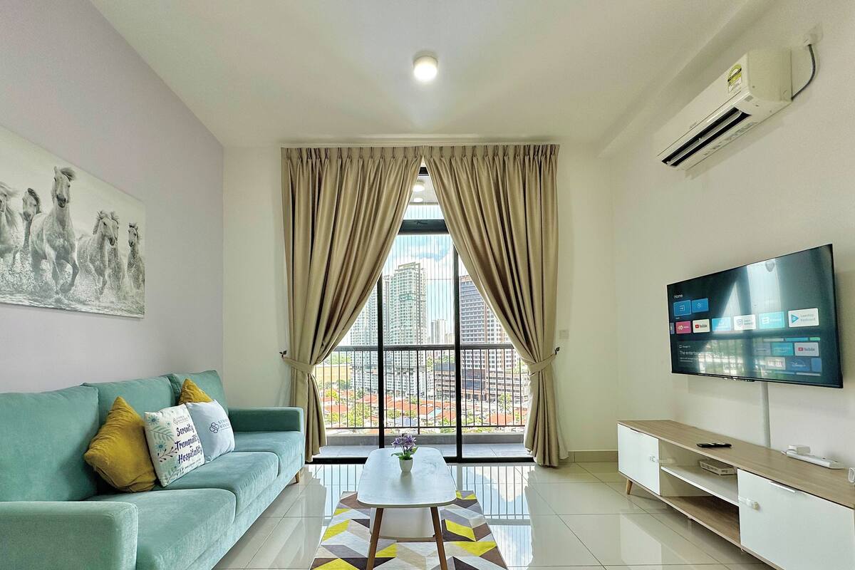 A modern living room with a sofa, a coffee table, a TV, and a large window with curtains.