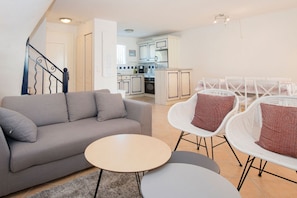 A modern living room with a sofa, two round tables, and white wicker chairs.