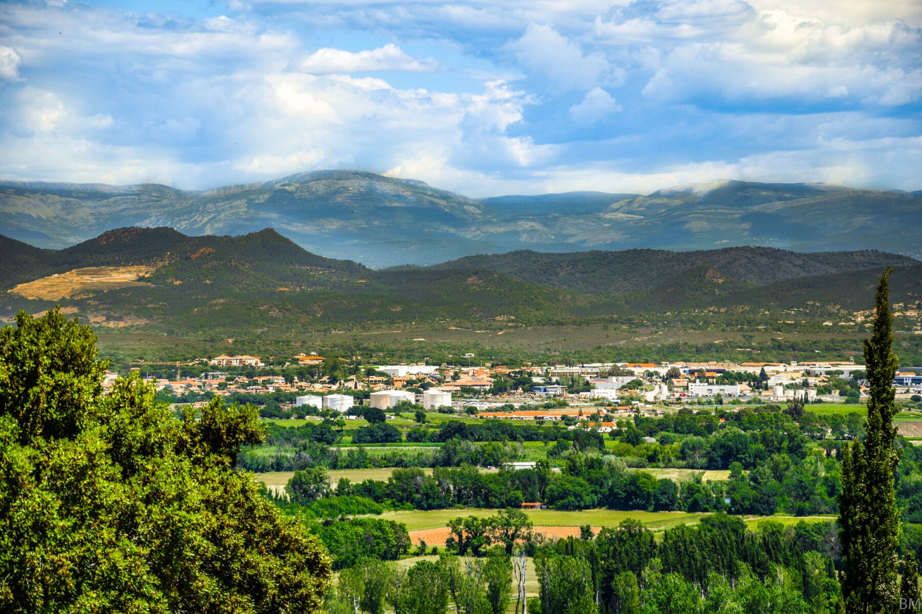 A town with buildings and green fields, surrounded by mountains.