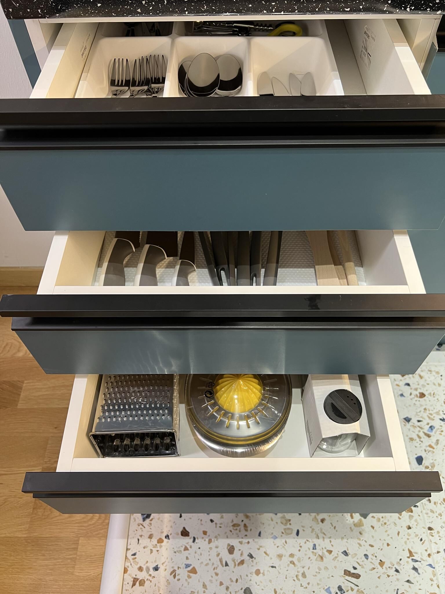 A kitchen drawer with utensils, a grater, and a spice rack.