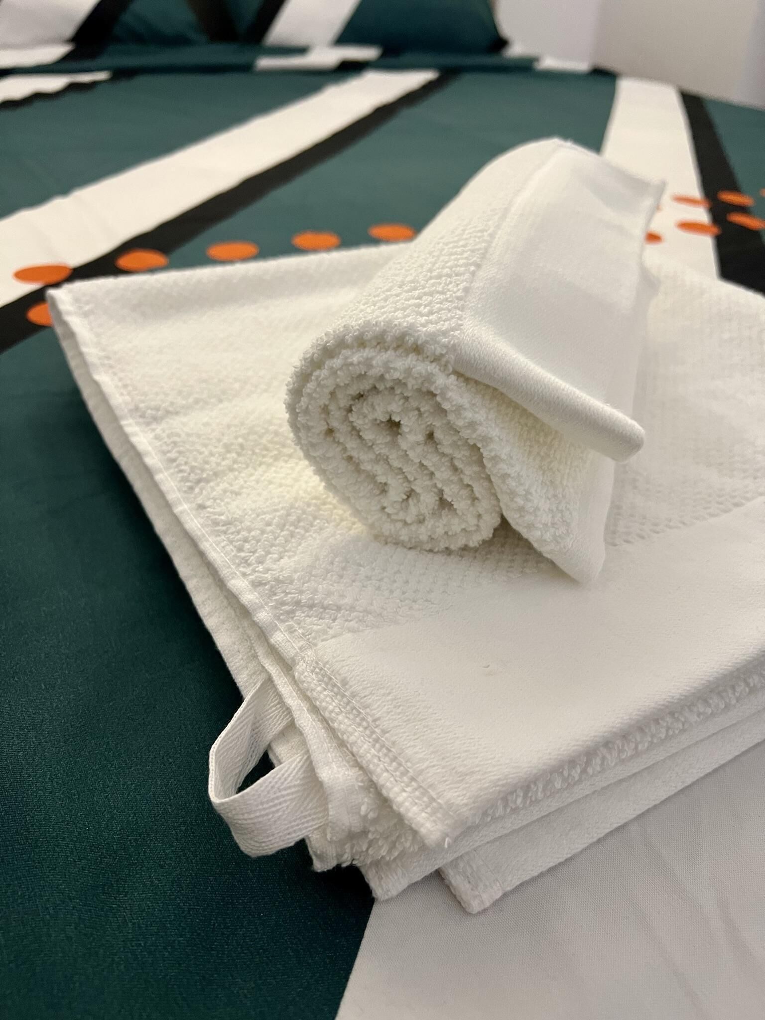 A neatly folded white towel on a green and white patterned bedspread.