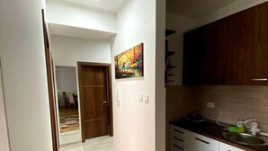A narrow hallway with a wooden floor, a patterned rug, a painting on the wall, and a kitchen area with cabinets and a sink. - Brand new 2 Bedroom Apartment in the Center Skopje (Skopje)