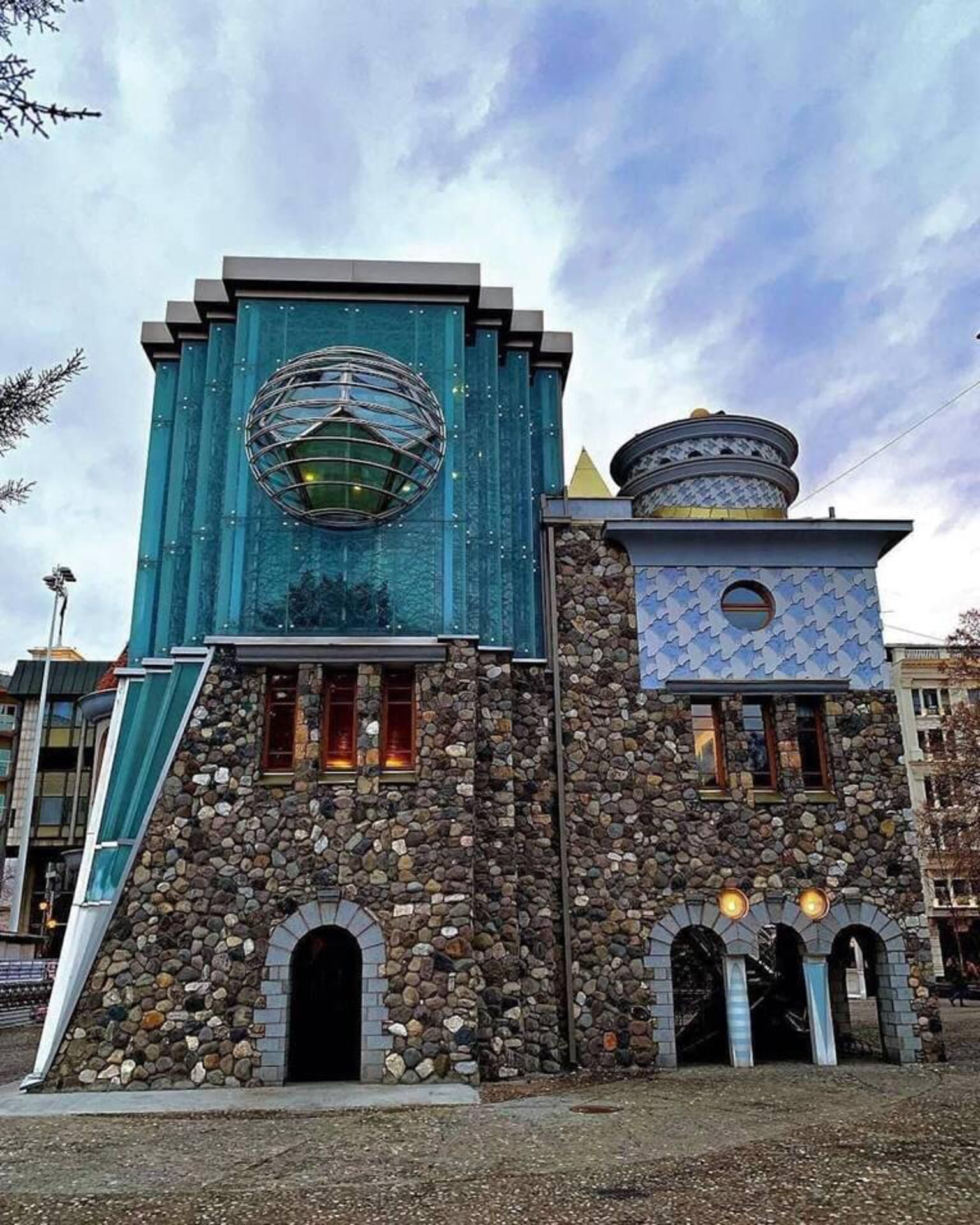 Un edificio con una grande struttura sferica al piano superiore, una facciata in pietra e una piccola finestra circolare al piano inferiore.