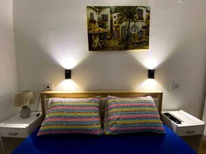 A bed with striped pillows, a nightstand with a lamp, and a painting on the wall. - Brand new 2 Bedroom Apartment in the Center Skopje (Skopje)