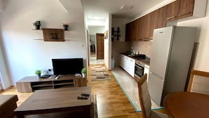 A modern kitchen with wooden cabinets, a refrigerator, and a countertop. There is a dining area with a table and chairs. - Brand new 2 Bedroom Apartment in the Center Skopje (Skopje)