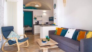 Ein Wohnzimmer mit einer Couch, einem Schaukelstuhl, einem Couchtisch und einer Küche im Hintergrund.