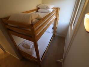 Uma cama beliche com roupa de cama branca num quarto com piso de madeira e uma janela.