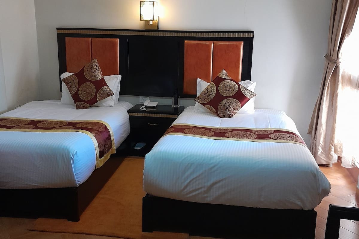 Ein Hotelzimmer mit zwei Betten, einem Fernseher, einem Nachttisch und einem kleinen Tisch mit einem Stuhl.