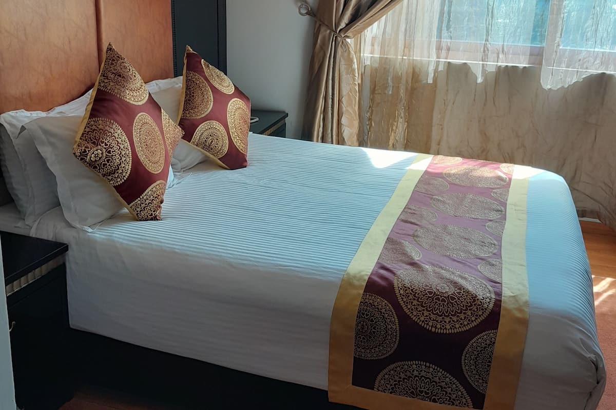 Ein Hotelzimmer mit einem großen Bett, einem Kopfteil, einem Nachttisch, einer Wandleuchte und einem Fenster mit Vorhängen.