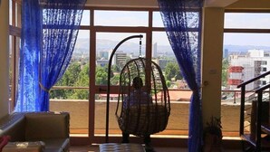 Una habitación con ventanas amplias, una silla de mimbre y vistas a un paisaje urbano.