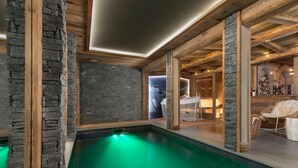 Ein Wellnessbereich mit Steinwand, Holzbalken und einem Pool in grüner Beleuchtung.