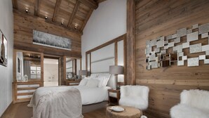 Ein geräumiges Schlafzimmer mit einem großen Bett, Holzboden und Blick auf eine verschneite Landschaft durch ein Fenster.
