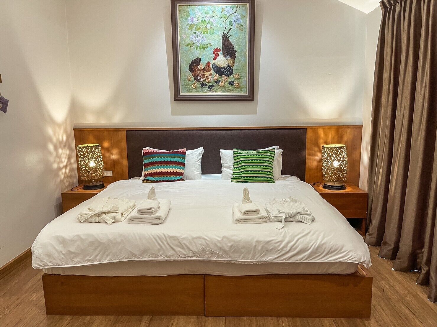 Una cama bien hecha con sábanas blancas, dos almohadas y una obra de arte enmarcada de un gallo sobre ella.