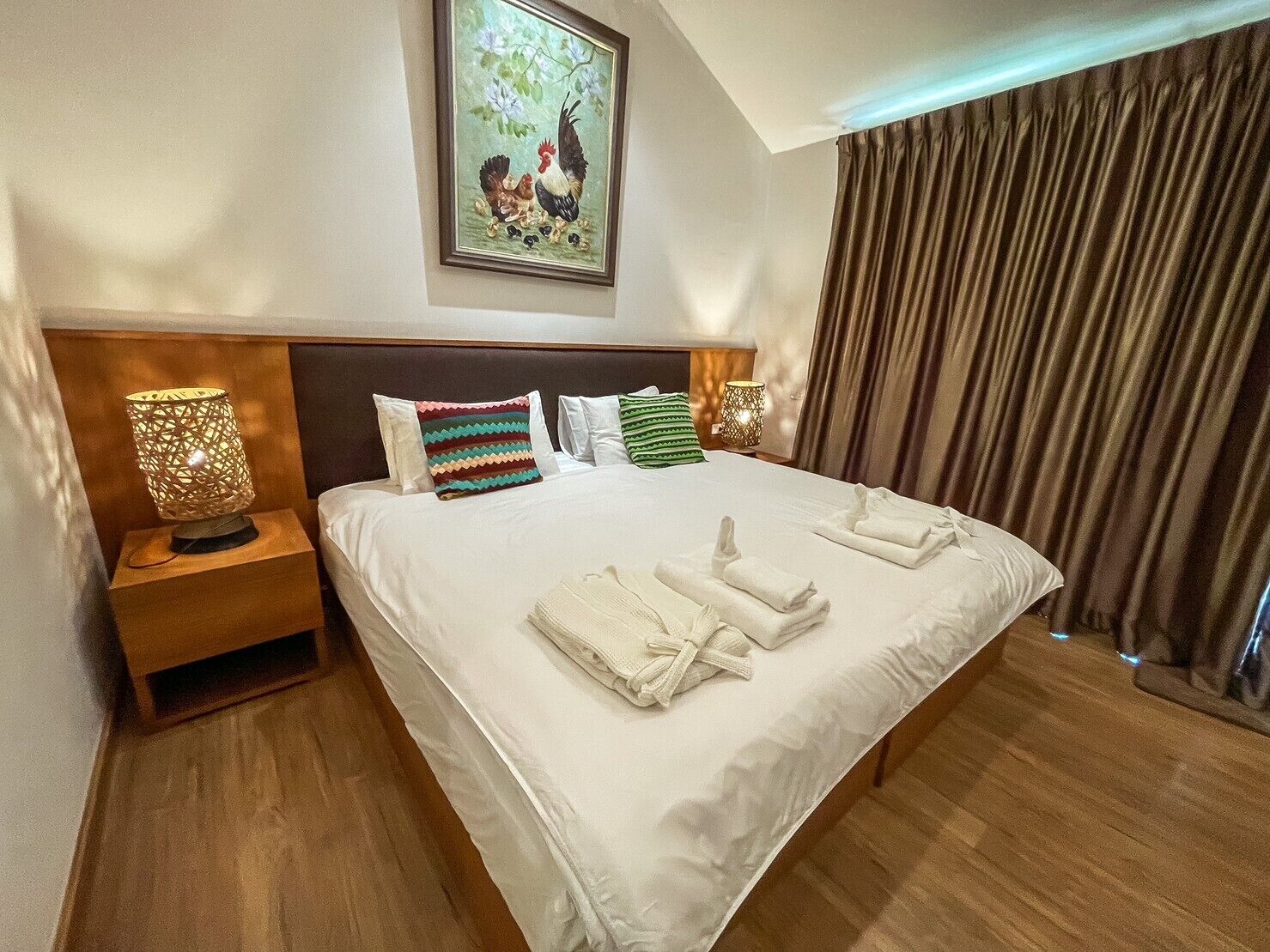 A hotel room with a large bed, two bedside tables with lamps, a framed picture on the wall, and a curtain on the window.