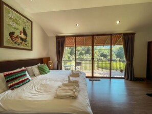 Relax in this inviting room with a large bed, framed artwork, and a balcony offering a view of lush greenery.