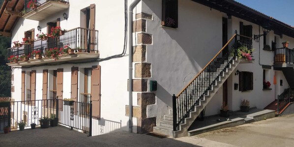 A two-story building with a staircase, balconies with flower boxes, and a door with a window. - Gartzinea, beautiful and spacious rural house in Ezkurra, north of Navarra (Ezcurra)