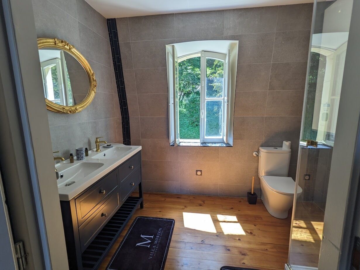 Een badkamer met twee wastafels, een toilet en een raam met uitzicht op groen.