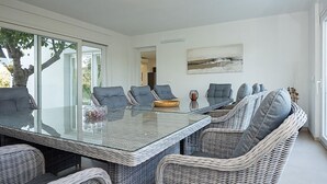 A modern dining area with a glass table surrounded by wicker chairs, a painting on the wall, and a view of the outdoors.