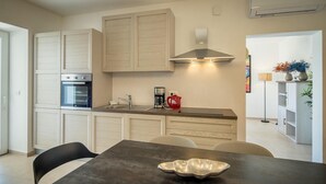 A modern kitchen with white cabinetry, a built-in oven, a coffee maker, and a dining table with a metal bowl.