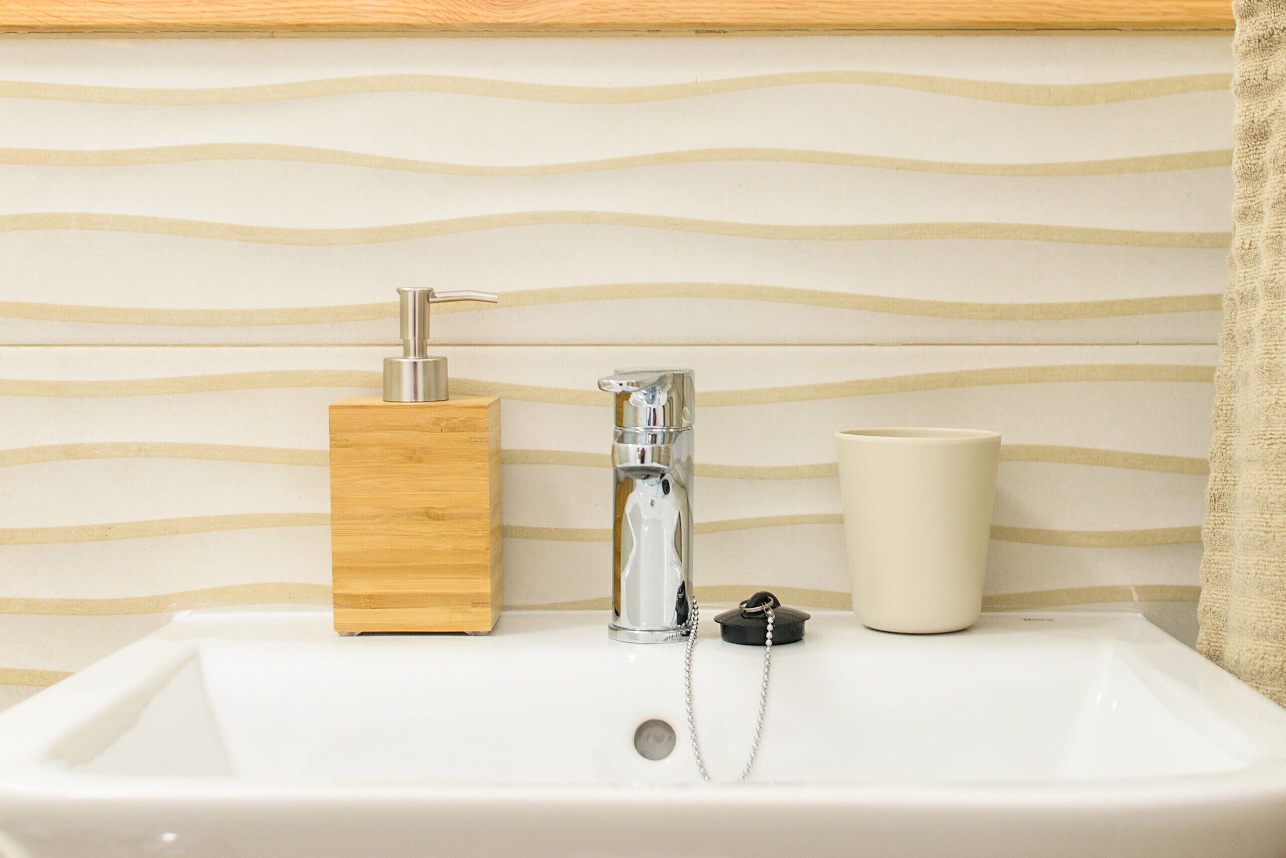 A bathroom sink with a wooden soap dispenser, a faucet, and a white mug.