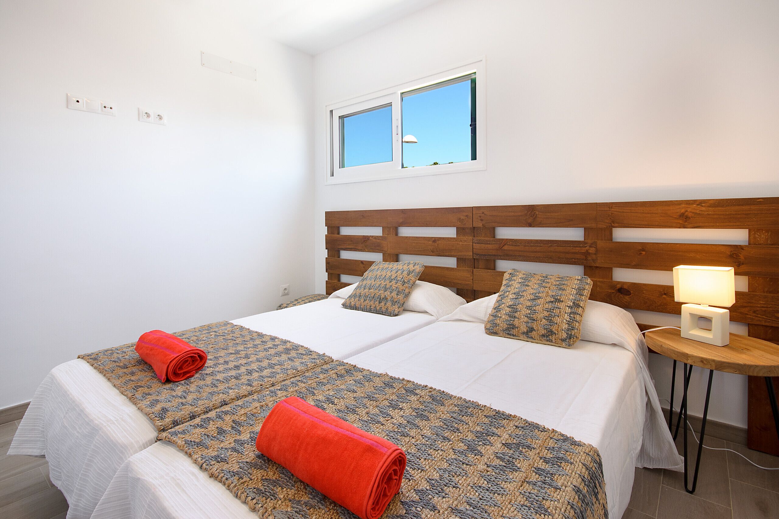 Una cama doble con cabecera de madera, dos mesitas de noche y una ventana con vistas al cielo.