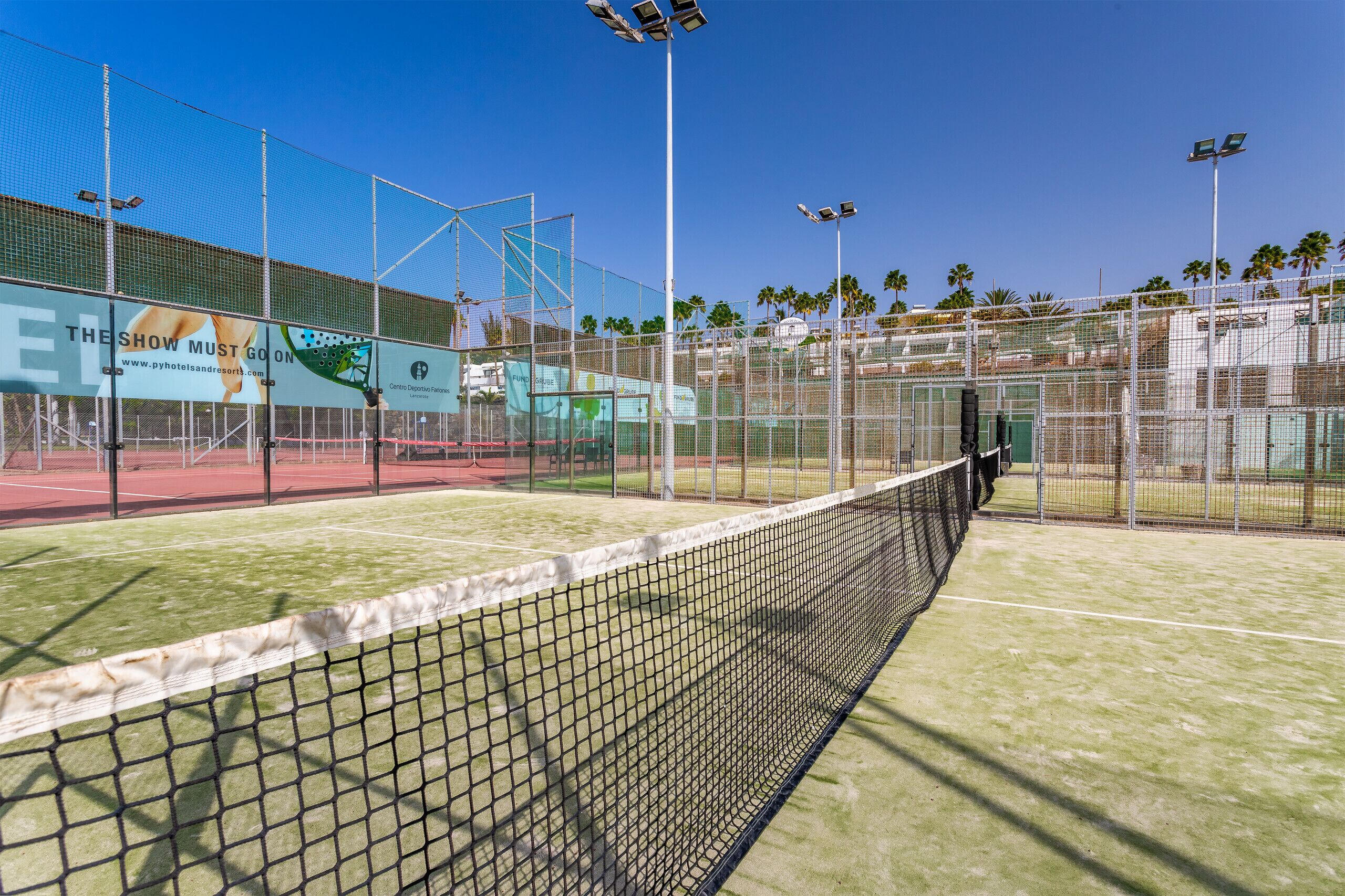 A tennis court with a net, surrounded by a fence, and advertising banners.