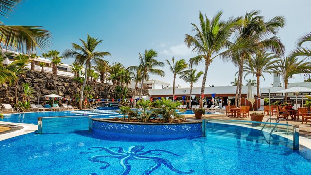 A swimming pool with a mosaic octopus design, surrounded by palm trees and lounge chairs. - Blue Volcano • Pool and Gym • Beach 1 min • LVH (Puerto del Carmen)
