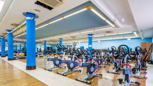 A gym with multiple exercise bikes and cardio machines, blue pillars, and a wooden floor. - Blue Volcano • Pool and Gym • Beach 1 min • LVH (Puerto del Carmen)