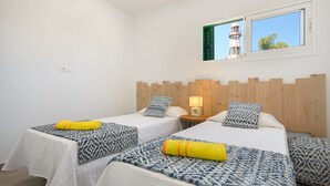 A hotel room with two beds, a wooden headboard, a window with a view of a lighthouse, and a small table with a lamp. - Orange Volcano • Pool and Gym • Beach 1 min • LVH (Puerto del Carmen)