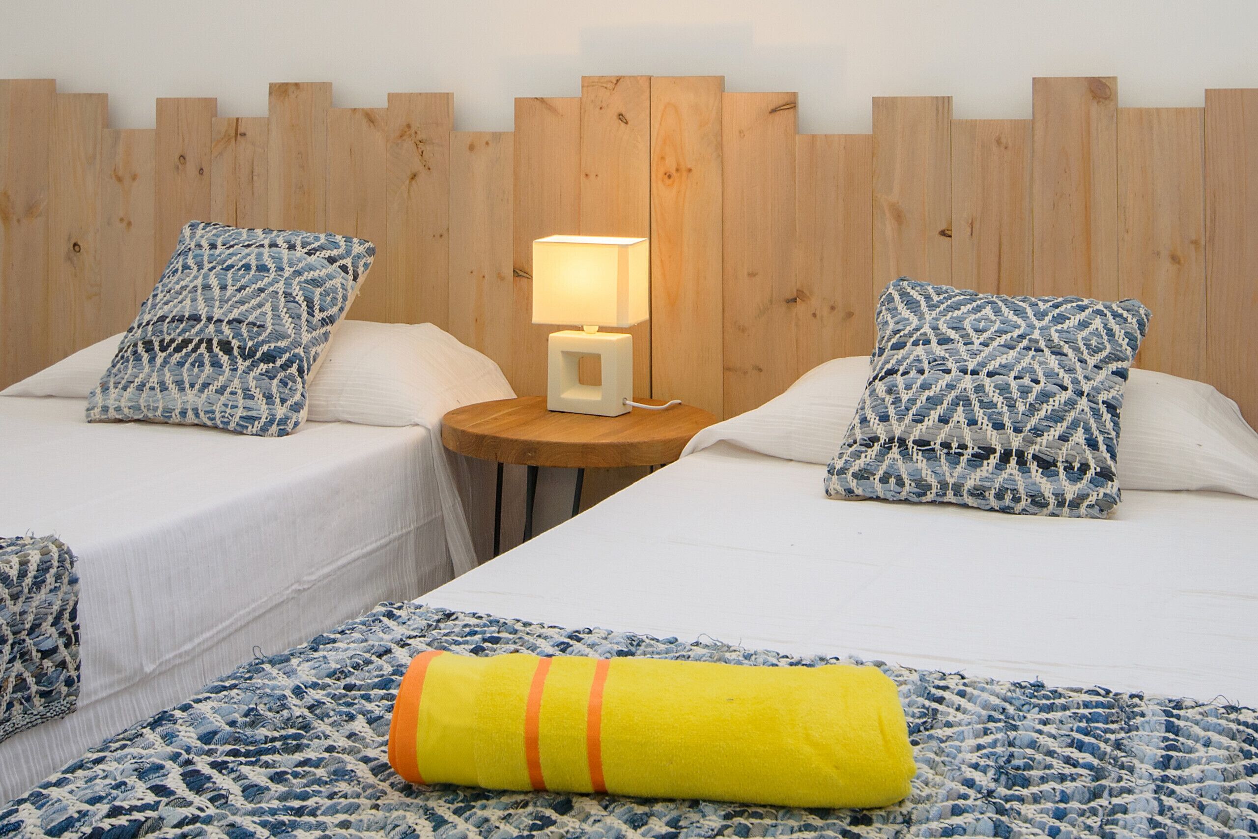 Ein Hotelzimmer mit zwei Betten, einem hölzernen Kopfteil und einem Nachttisch mit Lampe.